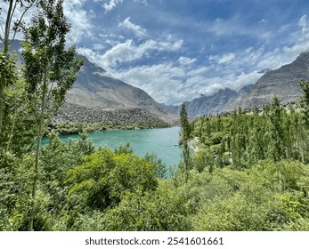 A serene turquoise lake surrounded by lush greenery and tall trees, with towering rocky mountains under a partly cloudy sky, creating a tranquil, pristine scene. - Powered by Shutterstock