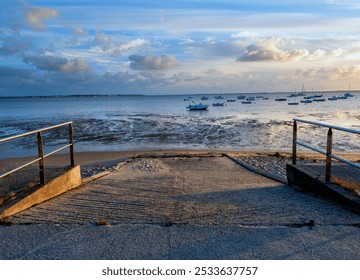 A serene view of a boat dock at sunset with boats anchored in the calm sea and a partly cloudy sky - Powered by Shutterstock