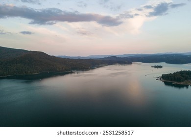 A serene view of a calm lake surrounded by lush green hills, reflecting the soft colors of twilight. A perfect escape for nature lovers and photographers alike. - Powered by Shutterstock