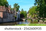 A serene view of a canal in Brugge, Belgium. Colorful buildings line the water, and a charming bridge arches over. The still water mirrors the sky, making it an ideal relaxing getaway.