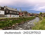 A serene view of the Glomma River flowing by historic wooden buildings in Roros, under a pastel-hued sky. Norway