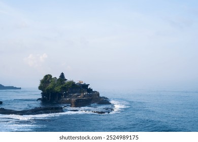 A serene view of the iconic Tanah Lot Temple perched on a rocky outcrop, surrounded by the ocean waves. Captured at dusk with the misty horizon and gentle waves. - Powered by Shutterstock