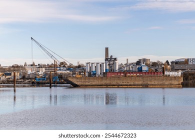 A serene view of an industrial waterfront area in Victoria, Vancouver Island, Canada, featuring a crane, warehouses, and calm water reflecting the cityscape. - Powered by Shutterstock