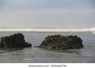 Serene view of a rocky shoreline with gentle ocean waves crashing in the background. A perfect depiction of nature's tranquility and the beauty of coastal landscapes. - Powered by Shutterstock