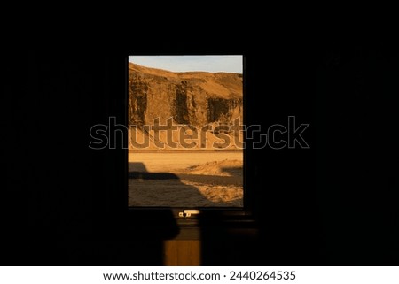 A serene view through a window frame the warm glow of sunset on desert cliff highlighting the beauty of arid landscape with light and shadow at cabin home in Iceland