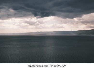 The serene waters of the Dead Sea lie under stormy skies, offering a dramatic and contemplative scene that draws visitors from around the world to witness the stark beauty and the stark contrasts