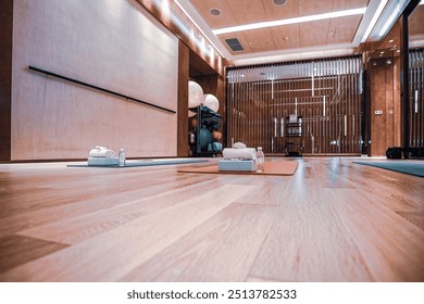 A serene and well-equipped yoga studio with a modern design, featuring hardwood flooring, wall-length mirrors, and warm lighting. The space is set up with yoga mats and props, ready for a session. - Powered by Shutterstock