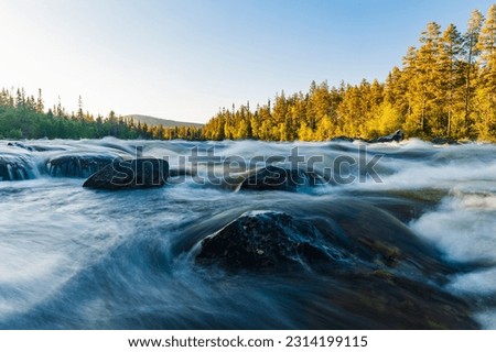 Serene wilderness: Norwegian river rushes, surrounded by trees, rocks and sky.