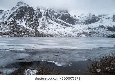 Serene winter landscape with snow-capped mountain, frozen lake, and overcast sky. Stark beauty and tranquility captured with no signs of life, Lofoten Island, Norway - Powered by Shutterstock