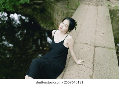 Serene Woman in Black Dress Relaxing on a Stone Bridge by Tranquil Water, Surrounded by Lush Greenery – A Peaceful Outdoor Scene. - Powered by Shutterstock