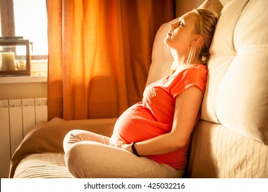 Serene woman during pregnancy relaxing at home with closed eyes. Sunlight is falling from window on woman face.