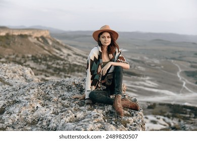 Serene woman in hat perched on rocky mountaintop amidst breathtaking mountain landscape - Powered by Shutterstock