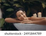 A serene woman with a relaxed expression enjoys a luxurious bath surrounded by lush greenery and soothing candlelight. Perfect for concepts of relaxation, self-care, and spa advertisements featuring