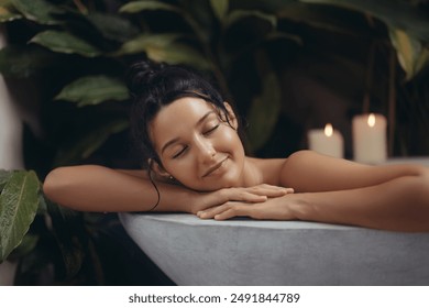 A serene woman with a relaxed expression enjoys a luxurious bath surrounded by lush greenery and soothing candlelight. Perfect for concepts of relaxation, self-care, and spa advertisements featuring - Powered by Shutterstock