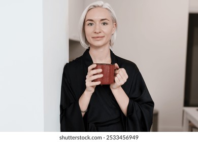 A serene woman with short blonde hair enjoys a warm cup of coffee indoors, exuding relaxation and calmness in a comfortable home environment. - Powered by Shutterstock