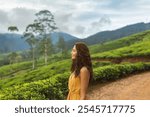 A serene woman in a yellow dress admires the beauty of lush tea plantations in Nuwara Eliya, Sri Lanka. The peaceful green hills and mountain backdrop create a perfect setting for travel, nature, and