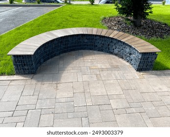 A serene wooden bench is placed in the middle of a brick path, providing a peaceful space to relax amidst greenery. The lush shrubs and grass enhance the tranquility of this outdoor setting - Powered by Shutterstock