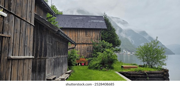 A serene wooden cabin nestled by a misty lakeside, surrounded by lush greenery and towering mountains shrouded in clouds. The tranquil atmosphere evokes a sense of peace and solitude. The rustic charm - Powered by Shutterstock