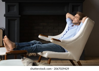 Serene Young Man Put Hands Behind Head, Feet On Footstool, Relaxing In Leather Comfortable Armchair In Luxury Home With Fireplace. No Stress, Fatigue Relieve, Furniture Store Ad, Peace Of Mind Concept