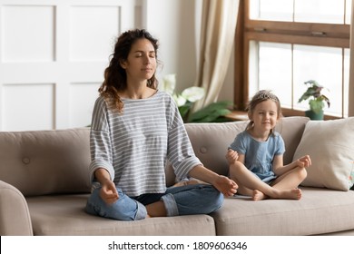 Serene Young Mother Her Little Adorable Daughter Meditating Breath Fresh Air Sitting Resting Cross-legged On Couch In Living Room. Healthy Lifestyle Yoga Practice, Parent Teach Kid Of Calmness Concept