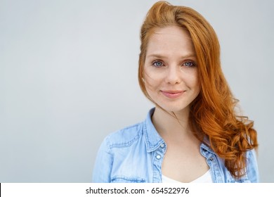 Serene Young Woman With A Quiet Relaxed Smile And Her Long Red Hair Over One Shoulder In A Head And Shoulders Portrait Over Light Grey With Copy Space