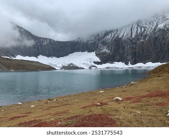 Serenene blue lake shrouded in misty clouds, nestled amidst snow-capped mountains and vibrant red flowers, nature’s perfect harmony - Powered by Shutterstock