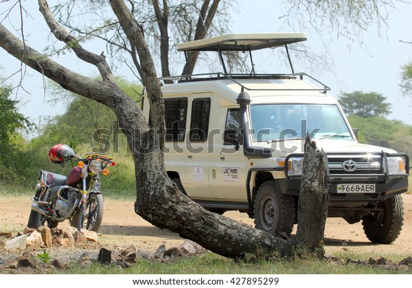 SERENGETI NATIONAL PARK, TANZANIA - JUNE 11: jeep\
and motorcycle parked under a tree on June 11, 2013 in Serengeti\
National Park. This famous and large area is visited by over 90000\
tourists per year