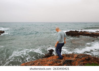 Serenity and strength man stands firm on rocks facing the crashing waves.