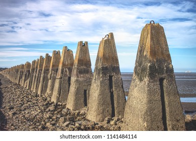 A series of concrete sea defenses, some partially broken down, at low tide. Photograph taken near Cramond Beach in Edinburgh, Scotland, United Kingdom. 