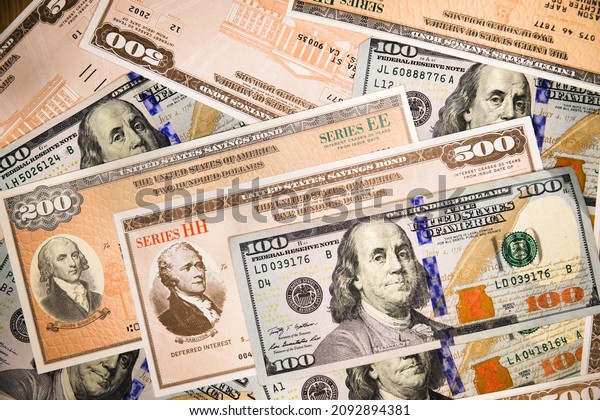 Series HH and Series EE United States Treasury\
Savings Bonds surrounded by US currency in cluding a $100 bill.\
Issued by the US Government and  purchased from the U.S. Department\
of the Treasury.