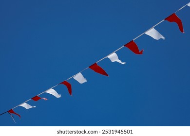 a series of small red and white triangular flags hanging from ropes, waving under the bright blue sky.
