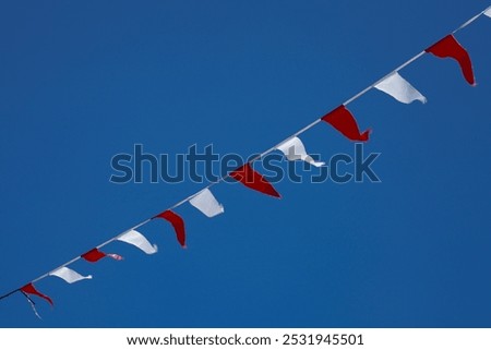 a series of small red and white triangular flags hanging from ropes, waving under the bright blue sky.