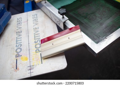 Serigraphy Silk Screen Print Process At Clothes Factory. Frame, Squeegee And Plastisol Color Paints.