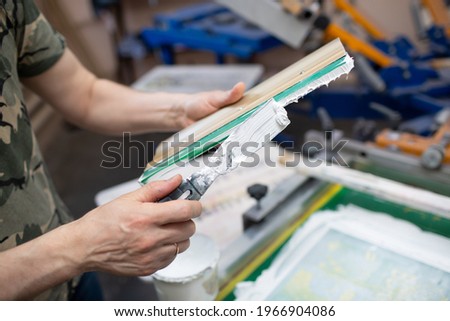 Serigraphy silk screen print process at clothes factory. Cleansing Frame, squeegee and plastisol color paints.