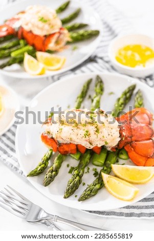 Sering garlic lobster tails with steamed asparagus and lemon wedges on a white plate.