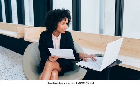 Serious 20 dark skinned female manager browsing web page on laptop computer during work in office, confident african american businesswoman making online research checking exchange and data