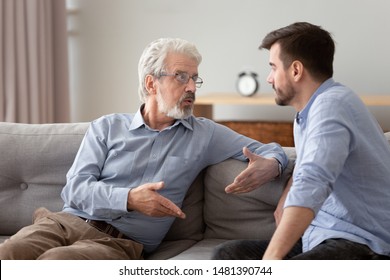 Serious 60s elderly father and grown up adult son sitting on sofa talking having important conversation trying to solve life issues problem, different men relative people communication at home concept