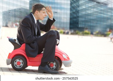 Serious Adult Businessman Sitting In The With Little Red Toy Car And Trying To See His Way