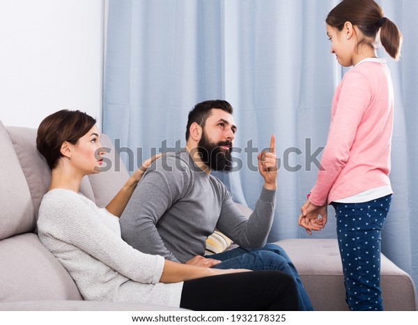 Serious adult father and mother telling off\
their daughter for\
disobedience