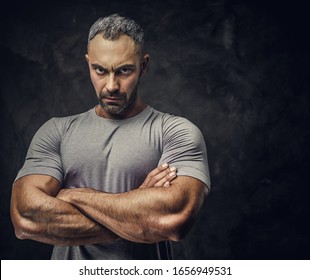 Serious, adult, fit muscular caucasian man coach posing for a photoshoot in a dark studio under the spotlight wearing grey sportswear, showing his muscles with arms crossed looking angry - Powered by Shutterstock