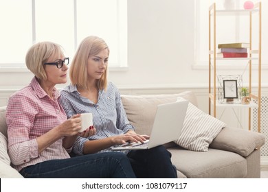 Serious Adult Mother And Daughter Drinking Coffee And Using Laptop, Reading News At Home. Generation And Relationship Concept