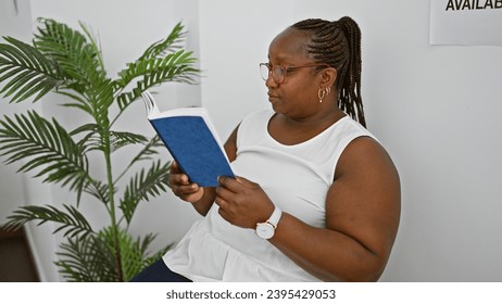 Serious african american business woman, sitting comfortably in a waiting room chair, engrossed in reading a book, projecting professional elegance and success. - Shutterstock ID 2395429053