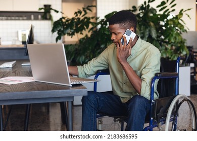 Serious African American Businessman With Disability Talking On Smart Phone And Using Laptop. Unaltered, Creative Business, Workplace, Physical Disability, Concentration, Technology.