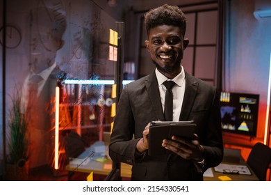 Serious African American Businessman Managing Project On Digital Tablet Pc, Working In Night Office With Scrum Glass Board. Focused Male Professional Planning Corporate Strategy Using Computer