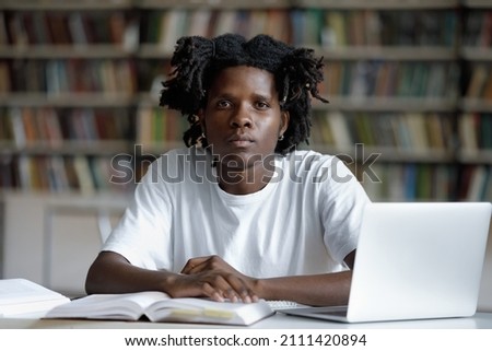 Serious African American college student with trendy dreads studying at table with laptop and summary notes in university library, sitting at desk, looking at camera. Head shot portrait