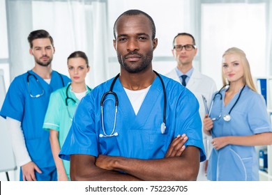 serious african american doctor with crossed arms with colleagues standing together on background
