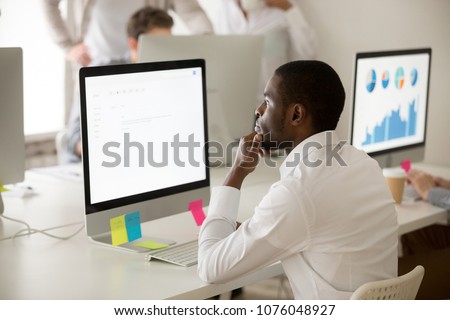 Serious african american employee thinking over business email working on computer in office, focused puzzled black manager looking at screen reading or writing electronic letter to corporate client