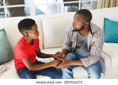 Serious African American Father And Son Sitting On Couch In Living Room Talking And Holding Hands. Family Spending Time At Home, Father Son Relationship.