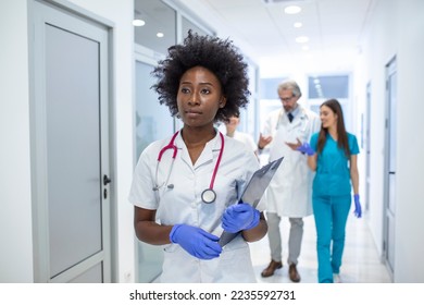 Serious African American female doctor walking with patient's test results before meeting with the patient. The doctor is in a hospital hallway. - Powered by Shutterstock