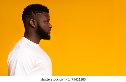 Serious african american guy profile portrait. Black man looking aside at copy space on yellow studio background